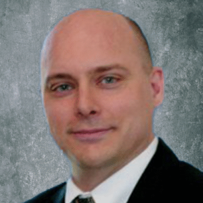 Professional man in suit smiling against a gray backdrop.