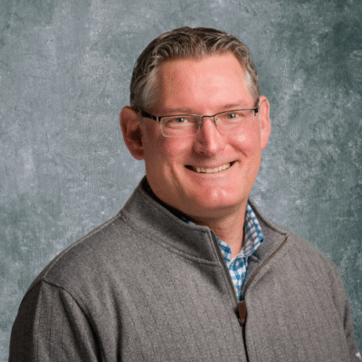 Smiling middle-aged man wearing glasses and a gray sweater.